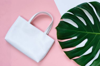 Tropik yeşil palmiye yaprağı ve pembe arka planda beyaz çanta. Canavar, şablonu, maketi bırakır. Yaz modası geçmişi.