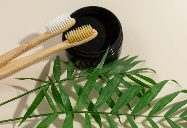 A set of eco-friendly bamboo toothbrushes and black tooth powder on a beige pastel background. Zero-waste, Sustainable lifestyle. Plastic-free concept