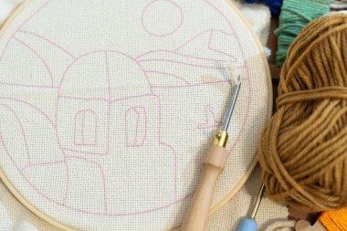 Bir zanaat alanında eskiz çizilmiş bir manzarayla nakış bir halka sergilenir. Gündüz vakti tekstil sanatında yaratıcılığı teşvik eden çeşitli iplikler ve araçlar yakınlardadır.