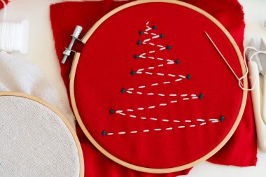 Evdeki bir el işi sırasında kırmızı bir halka şeklinde işlemeli Noel ağacı tasarımı. Kapat.