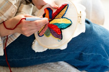 Kadın, canlı bir çiçek tasarımı içeren nakışlı bir parça üzerinde ustalıkla çalışıyor. Bu sanatsal aktivite kapalı bir yerde gerçekleşir, dinlendirici bir öğleden sonra yaratıcılığı yansıtır..