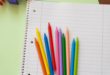 Parlak renkli boya kalemleri temiz, boş bir defter sayfasına yerleştiriliyor, sanatsal ifadeler ve yaratıcı oyunlar çağrıştırıyor. Çocuk sanat projeleri veya okul faaliyetleri için ideal.