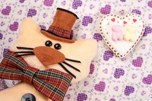 Zabawka kota w kapeluszu i muszka na poduszce obok piernika w formie serca i dwa niedźwiedzie — Zdjęcie stockowe