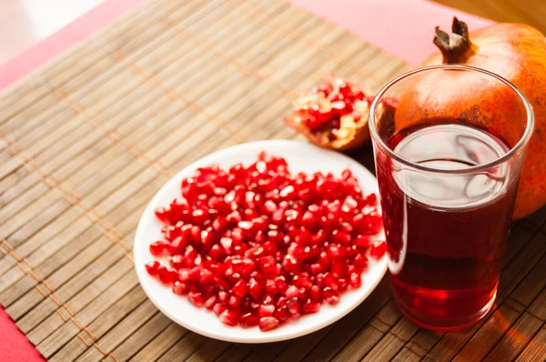 Grenades, half peeled pomegranate, pomegranate seeds on a white plate and a glass of garnet juice on a mat — Stock Photo, Image