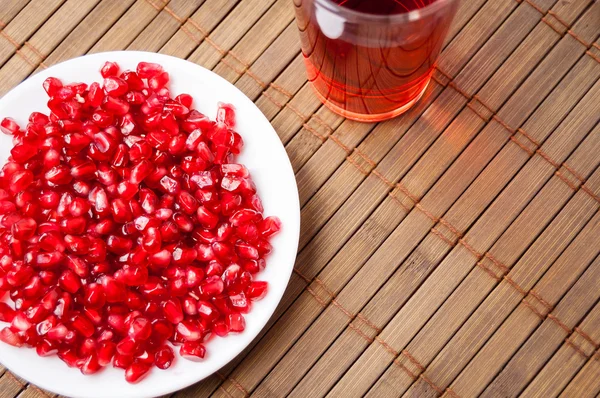 Granos rojos de granate en un plato blanco sobre una esterilla — Foto de Stock