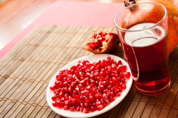 Grenades, half peeled pomegranate, pomegranate seeds on a white plate and a glass of garnet juice on a mat Stock Image