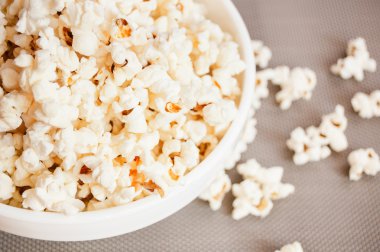 bir gri arka plan ve dökülmüş patlamış mısır üzerinde beyaz bir kase patlamış mısır