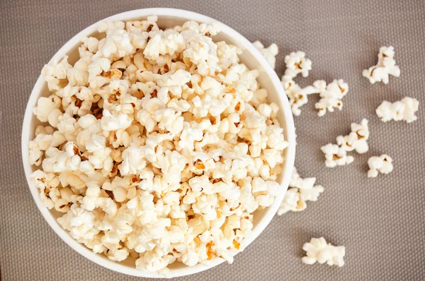 bir gri arka plan ve dökülmüş patlamış mısır üzerinde beyaz bir kase patlamış mısır