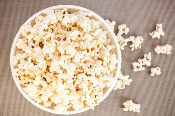 bir gri arka plan ve dökülmüş patlamış mısır üzerinde beyaz bir kase patlamış mısır