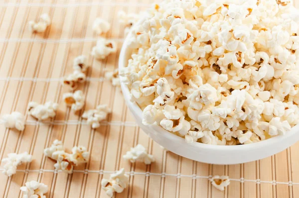 Palomitas de maíz en un tazón blanco y se derramó en la estera Imagen de stock