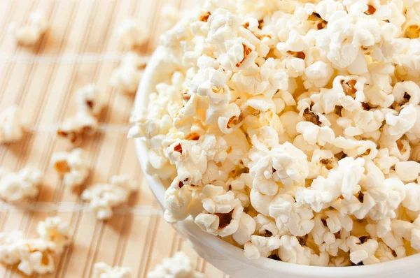 Popcorn in a white bowl and spilled on the mat Stock Photo