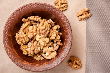 Kağıt ve gri arka plan üzerinde kahverengi çanak çömlek kapta ceviz taneleri