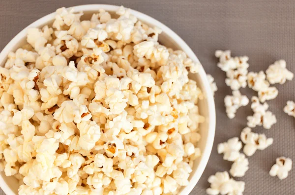 bir gri arka plan ve dökülmüş patlamış mısır üzerinde beyaz bir kase patlamış mısır