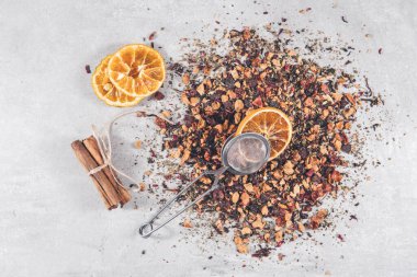 Kurutulmuş çiçek yaprakları ve tarçınlı böğürtlen, kuru portakal dilimi ve zerk makinesinden oluşan meyve çayı gri masada filtre.