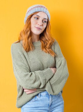 Kollarını kavuşturup poz veren ve taraf arayan genç bir kadın. Ayakta duran güzel bir kız, yarım boy, sarı arka planda soyutlanmış. Stüdyo çekimi