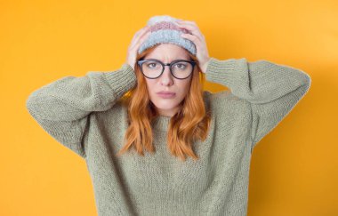 Yanlışlık. Kollarını başının üstünde tutan endişeli genç bir kadın, sarı arka planda izole edilmiş. Stüdyo çekimi