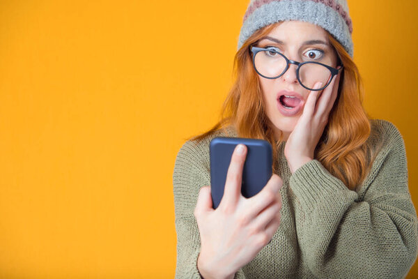 Испуганная молодая девушка с мобильным телефоном, изолированная на желтом фоне. Шокированная женщина. Не может быть. Снимок студии