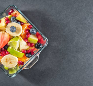 Koyu gri siyah masada gözlük kasesinde meyve salatası.