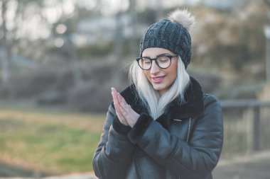 Ellerini ısıtan, kalın giysiler giyen genç bir kadın, Kasım ayı açık havada. Şirin kız üşüyormuş. Kış konsepti Soğuk havada bir kadın..