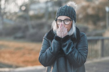 Ellerini ısıtan, kalın giysiler giyen genç bir kadın, Kasım ayı açık havada. Şirin kız üşüyormuş. Kış konsepti Soğuk havada bir kadın..