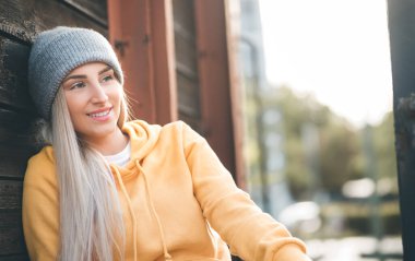 Gülümsemenin yarısı kadar genç ve güzel bir kadın yan bakmak istiyor. Açık havada gün ışığı. Olumlu duygularla gülümseyen güzel kız, gülen surat. Sıradan kıyafetler giyen bir kadın. Dışarıda.