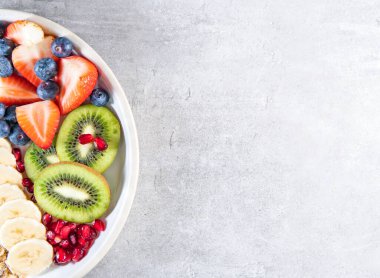 Bir dilim kivi, muz, çilek ve yabanmersini, tabakta meyve salatası. Gri masada sağlıklı bir yemek.