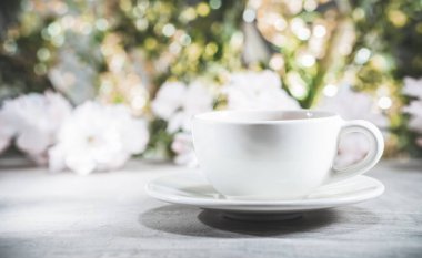 Çiçeklerin ve yaprakların bulanık arka planının önündeki çay fincanı. Bokeh konsepti - seçici odak