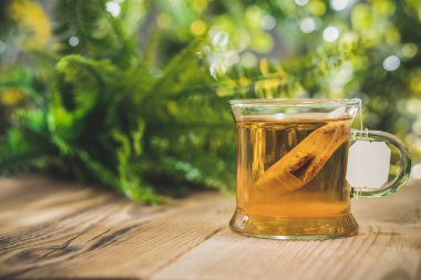 Çiçekli bahar bahçesinin önündeki tahta masanın üzerinde çay poşeti olan çay fincanı. Açık havada bokeh ışığı var. Ön görünüm