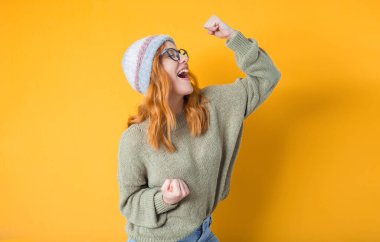Profile of excited young girl with closed eyes and clenched fists, isolated on yellow background. Yes concept. Good news. Pretty woman celebrates success. Studio shot