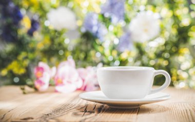 Çiçekli bahar bahçesinin önündeki ahşap masanın üzerinde bokeh ışığı olan çay fincanı. Ön görünüm