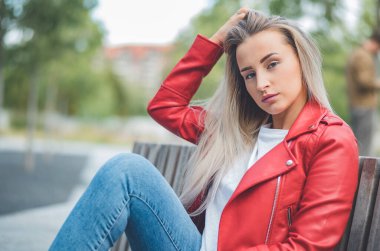 Parkta bankta oturan genç ve güzel bir kadın. Açık havada gün ışığı. Rahat kıyafetler giyen güzel bir kız. Dışarıda.