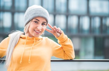 Yakın plan genç kadın barış şarkısını parmaklarıyla söylüyor. Açık havada gün ışığı. V işareti yapan hoş bir kadın. Dışarıda.