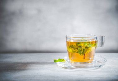 Gri arka planda cam fincanda yaprakları olan nane çayı, ön manzara. Reklamınız ya da mesajınız için boş bir alan. Kopyalama alanı
