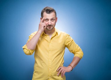 Kurnaz genç adam soruyor. Uzayı mavi arkaplana kopyala, sarı gömlekli giyin. Sor konseptinde yarı uzunlukta bir adam. Stüdyo çekimi