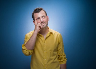 Katı genç adam düşünür. Mavi arka planda şaşkın surat ifadesi olan, sarı gömlekli şüpheli bir adamın portresi. Dikkatli ol adamım, mesaj için uzayı kopyala. Stüdyo çekimi