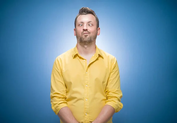 一个滑稽的男人 满眼傻笑 在蓝色的背景上嬉笑着 穿着黄色的衬衫 看起来傻傻的 疯狂的家伙 工作室拍摄 — 图库照片