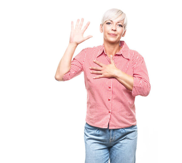 Я клянусь. Взрослая женщина делает ругательный жест и держит руку на груди, глядя на камеру, изолированную на белом фоне. Присягу на верность. Снимок студии