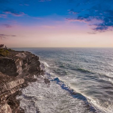 Sahil ve deniz, inanılmaz kayalık kıyılar. Taşlaşmış sahil üzerinde gün batımı ve kayalık kıyılara vuran tatlı okyanus suyu. Huzursuz mavi deniz. Atlantik Okyanusu - Portekiz