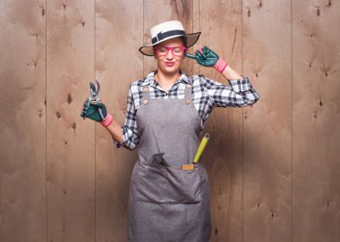 Gürültü - yüksek. Stüdyodaki ahşap arka planda gözlerini kapatan, elinde budama makası tutan kızgın, genç bir bahçıvanın yakın plan portresi. Stüdyo çekimi