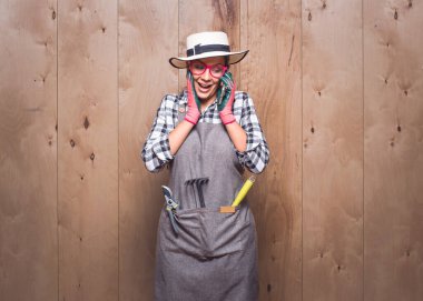 Kendinden geçmiş genç bahçıvan kadın stüdyoda ahşap arka planda akıllı telefondan konuşuyor. Cep telefonunu kullanan harika bir kadın çiftçi. Stüdyo çekimi