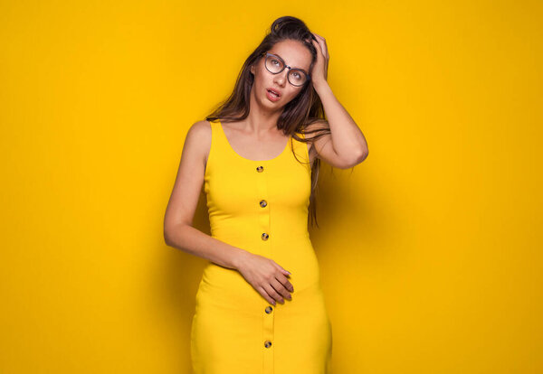 Bored young woman looking up while search an idea, isolated on yellow background. Girl forget something. Studio shot