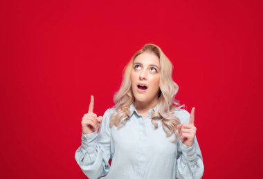 Yukarı bakan ve işaret eden genç bir kadın, kırmızı arka planda izole edilmiş, ürün tanıtımcısı kız alanınızı gösteriyor. Stüdyo çekimi