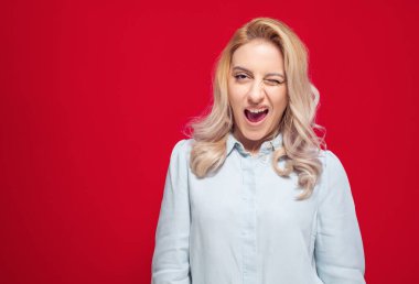 Mutlu kadın bir gözünü kırpıyor, kırmızı arka planda izole edilmiş. Neşeli bir kızın göz kırpışının stüdyo çekimi. Stüdyo çekimi