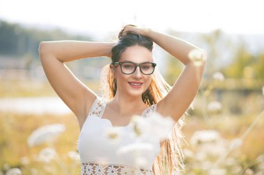 Gülümseyen genç bir kadın dışarıda kameraya bakıyor. Yarım boy. Çimlerde poz veren güzel bir kadın. Olumlu duygularla, gülen bir ifadeyle. 30 'lu yaşlardaki kadın