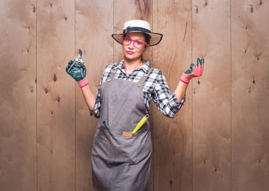 Bahçıvan kadının elinde budama makası stüdyoda ahşap arka planda parmaklarını şıklatıyor. Neşeli dişi çiftçi hareketleriyle klik yapıyor. Stüdyo çekimi