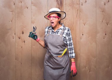 Stüdyoda ahşap arka plana bakarken elinde budama makası tutan, bağıran ve bağıran agresif genç bahçıvan kadın. Stüdyo çekimi