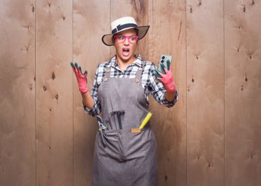 Kızgın bahçıvan kadın stüdyoda ahşap arka planda cep telefonuyla konuşuyor. Şımarık akıllı telefonu elinde tutan öfkeli kadın çiftçi, bir sorun var, sorun. Stüdyo çekimi