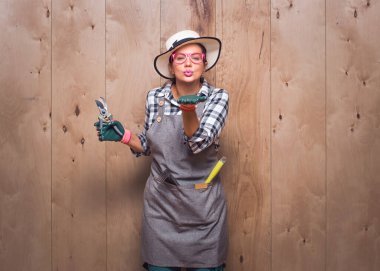 Güzel, genç bahçıvan kadın elinde budama makası tutarken stüdyodaki ahşap arka planda avucundan sana bir öpücük yolluyor. Aşk konsepti. Güzel kadın çiftçi. Stüdyo çekimi