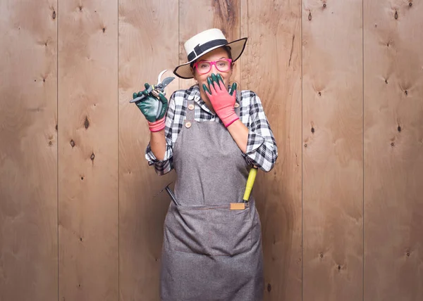 Şaşırmış kadın çiftçi stüdyoda ahşap arka planda kameraya bakıyor. Neşeli genç bahçıvan kadın elinde budama makası ile ağzını eliyle kapatıyor. Stüdyo çekimi