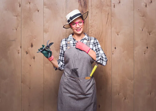 Stüdyoda tahta arka planda kameraya bakan güzel bir kadın çiftçi. Gülümseyen bir ifadeyle budama makası tutan mutlu bahçıvan kadının portresi. Stüdyo çekimi